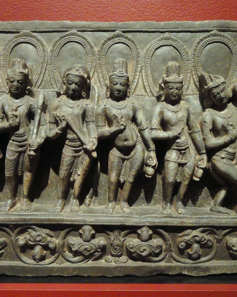A carved schist panel of the nine planetary deities standing in a row, each under an arch.