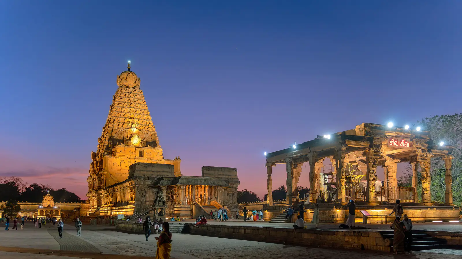 The great tower of the Brihadisvara Temple lit at dusk, the Nandi pavilion in the foreground
