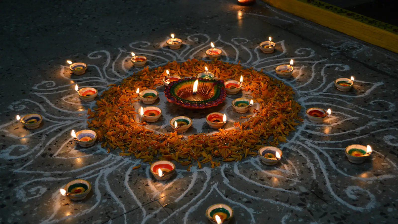 A ring of small lit clay lamps around a larger one, set in a white rangoli pattern