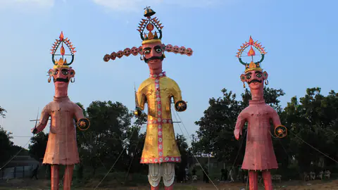 Three tall painted effigies with moustaches and crowns standing in a field before they are burnt on Vijayadashami