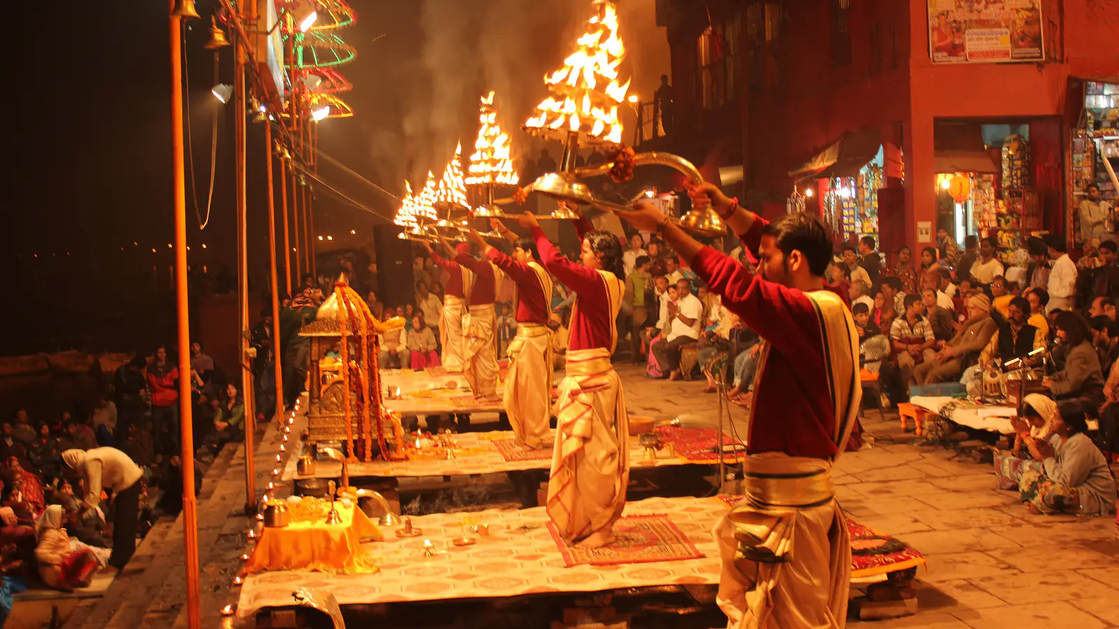 A row of priests on raised platforms raise tiered brass lamps in unison during the evening Ganga aarti