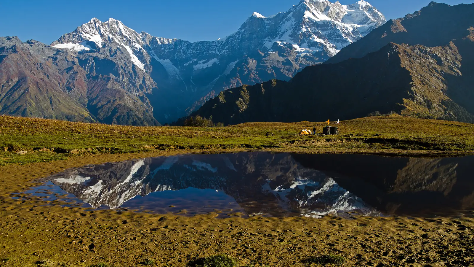 Snow peaks of Chaukhamba reflected in a still mountain pond on a high meadow