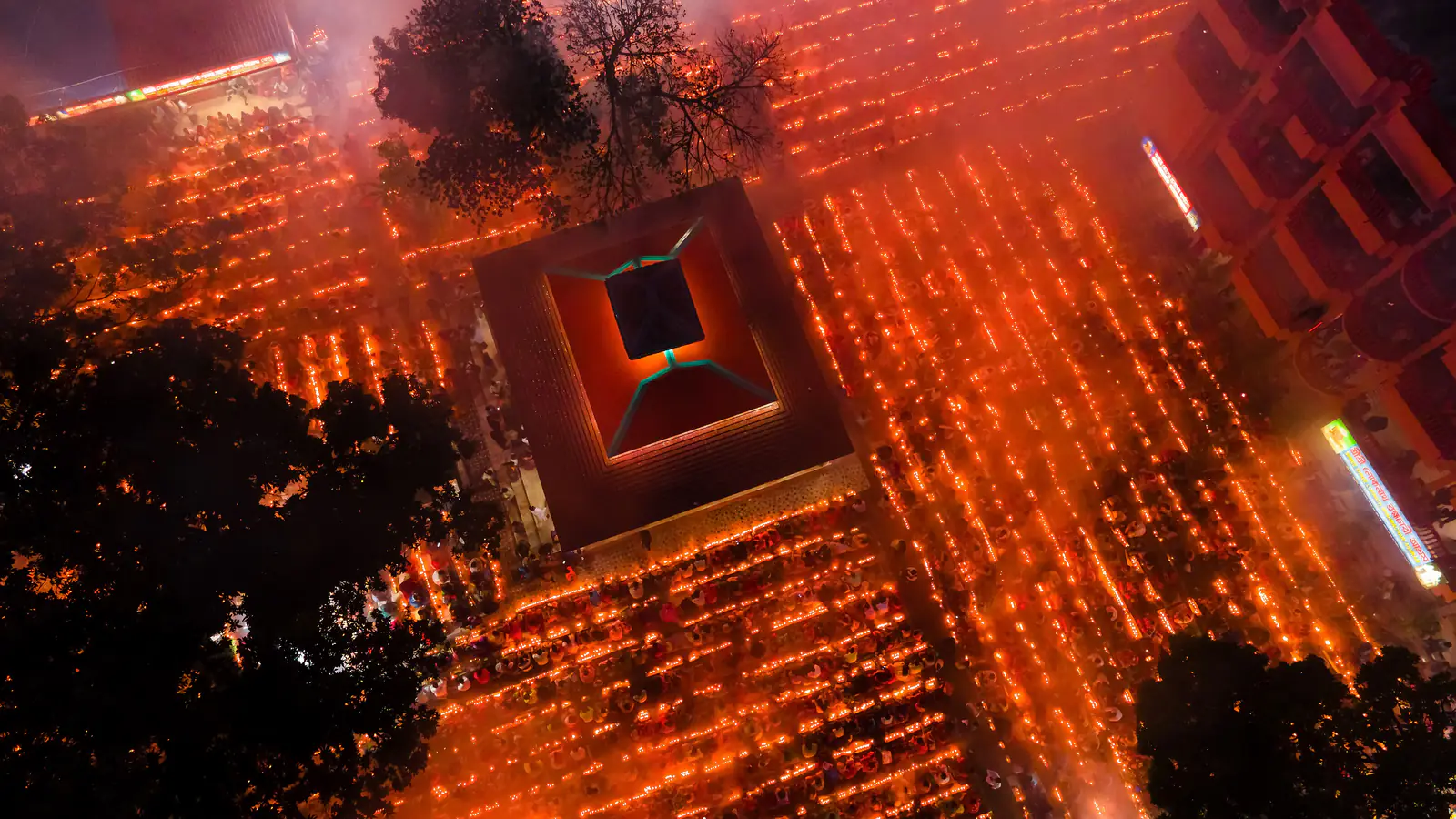 Seen from above at night, thousands of small oil lamps in rows fill a temple courtyard with warm light