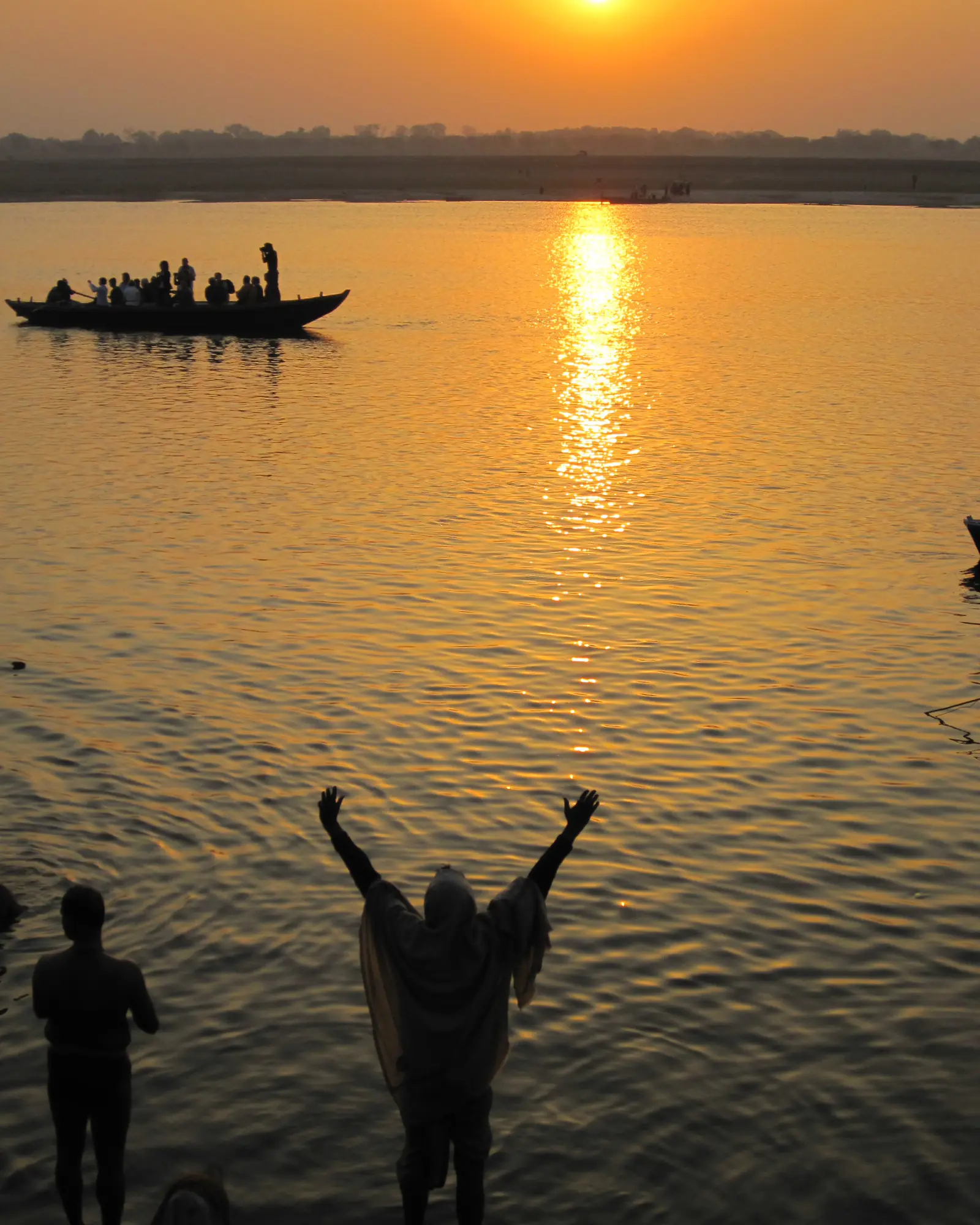 Silhouettes of people with raised arms facing a low sun over the river at dawn