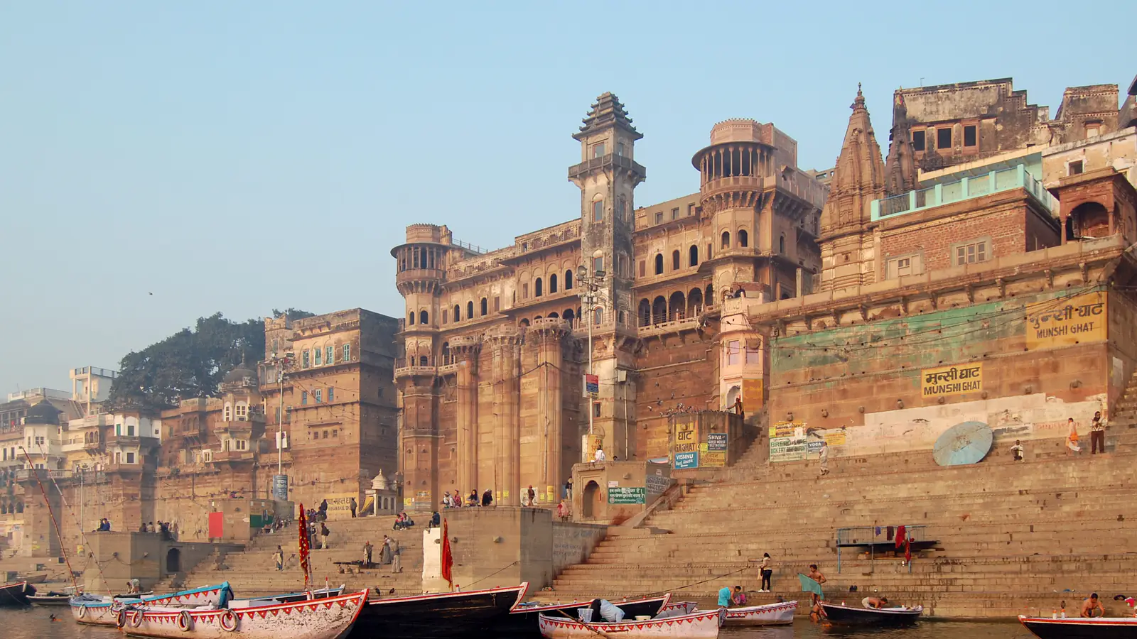 Stone steps and old palaces of Munshi Ghat rising from the river Ganga at Varanasi, boats moored below
